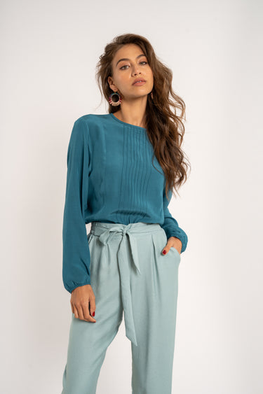 Woman wearing a teal top and light blue pants on a white background