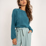 Woman wearing a teal top and light blue pants on a white background