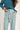 Person wearing a teal ribbed sweater and light blue pants on a white background