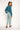 Woman wearing a teal top and light blue pants on a white background