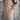Person wearing a long beige knitted dress with a belt against a neutral background