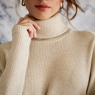 Close-up of a person wearing a beige turtleneck sweater with a blurred background